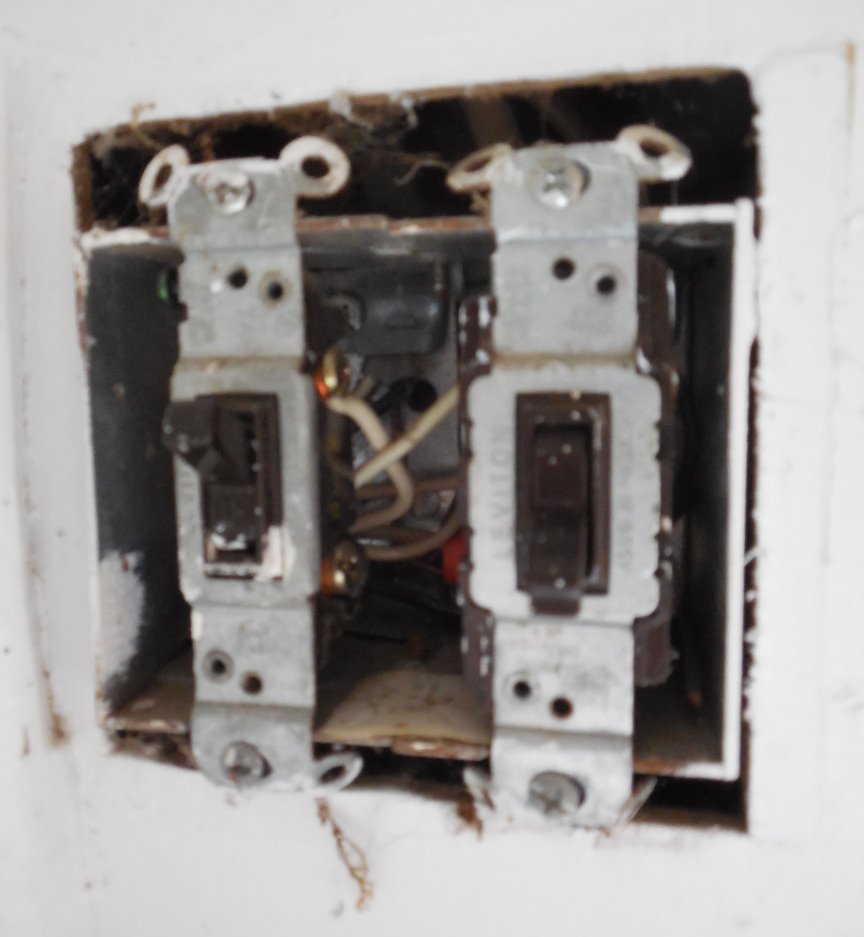 We see a white wall. In it we see a 
	metal switch box containing two toggle switches. There is a substantial
	opening between the cut edge of the wall and both the top and the bottom
edges of the switch box. From the cover's impression in the paint, you can tell
that before I removed the wallplate, it hid the dangerous gap.